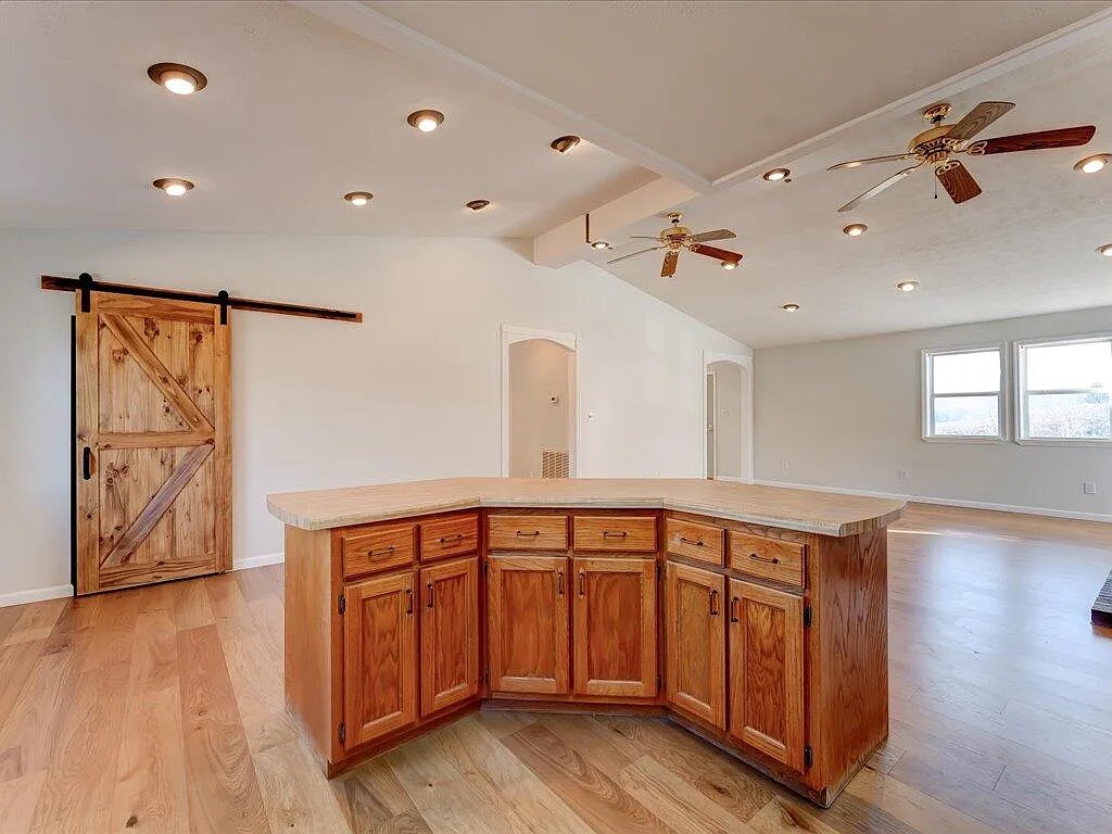 Vaulted great room with rustic barn door and oak island on new hardwood flooring