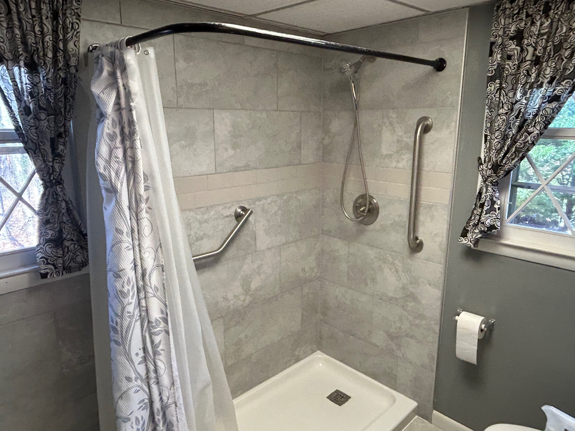 Renovated walk-in tile shower with grab bars and curved curtain rod