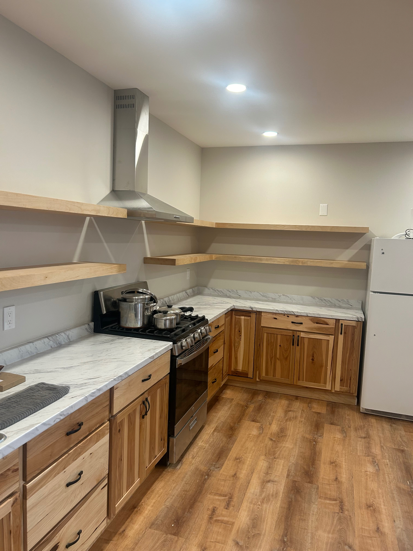 Hickory kitchen with floating shelves, marble countertops, stainless hood, and luxury vinyl plank flooring